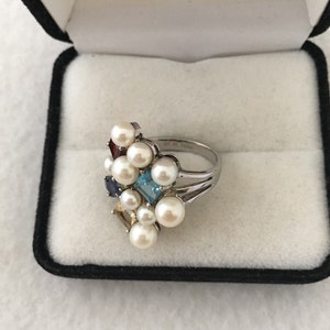May include: A silver ring featuring a cluster of white pearls and colourful gemstones, including blue, red, yellow, and green.