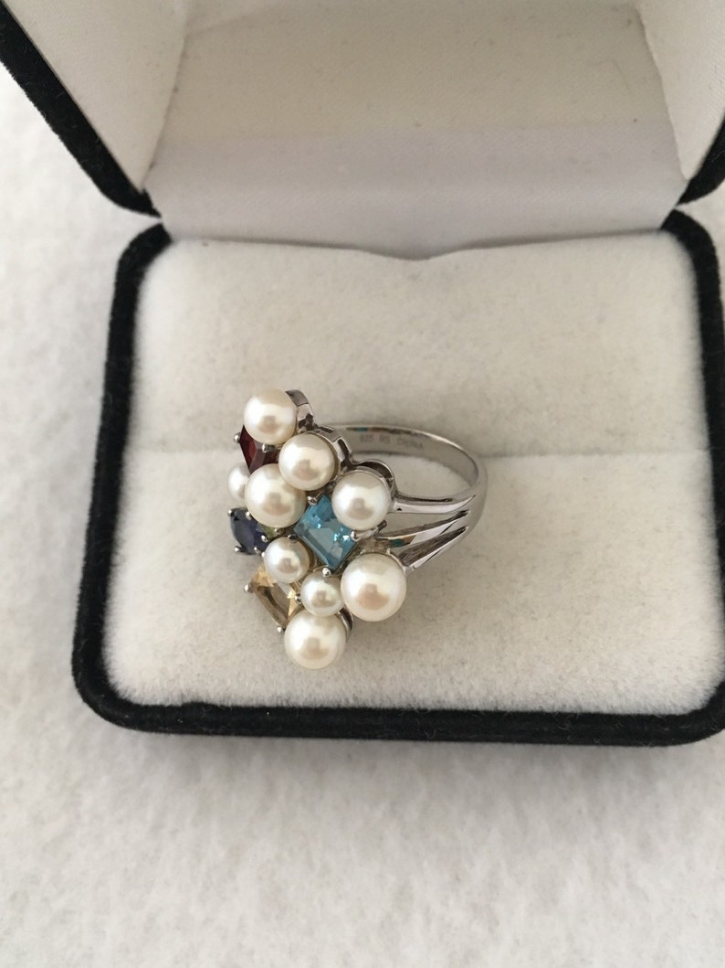 May include: A silver ring featuring a cluster of white pearls and colourful gemstones, including blue, red, yellow, and green.