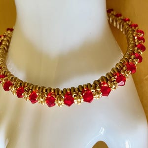 May include: A gold-toned bracelet with a double-strand design. The bracelet is adorned with vibrant red, faceted beads. The beads are evenly spaced along the bracelet's circumference, creating a striking contrast against the gold color.
