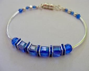 May include: A silver bangle bracelet with a row of blue square-shaped beads.