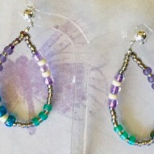 May include: A pair of teardrop-shaped earrings made with silver-colored beads, purple beads, white beads, and turquoise beads.