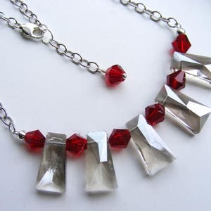 May include: A silver chain necklace with a silver clasp. The necklace has red and clear crystal beads. The clear beads are rectangular and faceted. The red beads are round and faceted.