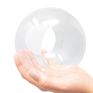 K&ouml;nnte beinhalten: Eine klare Glaskugel mit einem Loch in der Mitte, gehalten in der Hand einer Person.