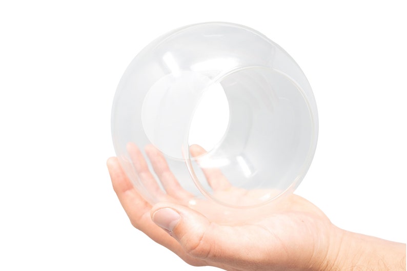 K&ouml;nnte beinhalten: Eine klare Glaskugel mit einem Loch in der Mitte, gehalten in der Hand einer Person.