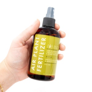 May include: A brown bottle with a yellow label that reads "Air Plant Fertilizer". The label also includes the text "Low-Nitrogen Fertilizer for Tillandsia & Other Epiphytes" and "16-9-25". The bottle is 8 fl oz.