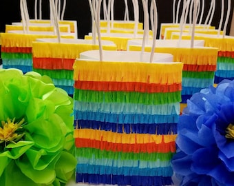 May include: A group of colorful paper bags with fringe trim, resembling a pinata. The bags have white handles and are decorated with stripes of yellow, orange, red, green, blue, and purple.