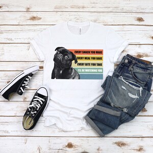 May include: White t-shirt with a black pug dog graphic and the text "EVERY SNACK YOU MAKE EVERY MEAL YOU BAKE EVERY BITE YOU TAKE I'LL BE WATCHING YOU" in a retro rainbow design.