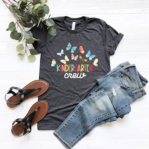 May include: A dark grey t-shirt with a rainbow colored "kindergarten crew" text and a design of colorful butterflies.