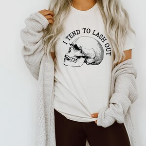 May include: White t-shirt with a black skull graphic and the text "I tend to lash out".
