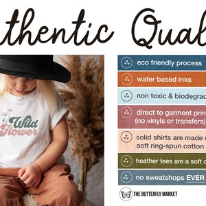 May include: A white t-shirt with a green and pink graphic that says "Wild Flower". The shirt is being worn by a child. The image also includes a list of details about the shirt's quality, including eco-friendly processes, water-based inks, and non-toxic materials.