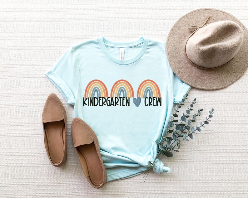 May include: A light blue t-shirt with three rainbow arches and the text "Kindergarten Crew" with a heart between the words.
