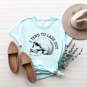 May include: A light blue t-shirt with a skull graphic and the text "I tend to lash out".