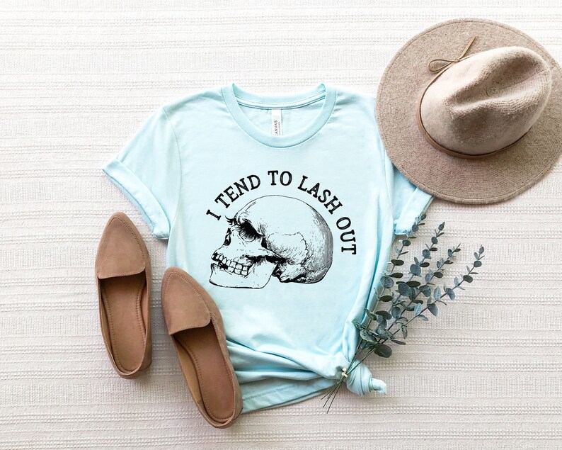 May include: A light blue t-shirt with a skull graphic and the text "I tend to lash out".