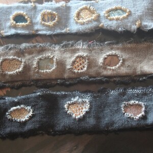 Può includere: Tre strisce di tessuto con colori e trame diverse. Ogni striscia ha diversi piccoli patch rotondi ricamati con colori e motivi diversi.