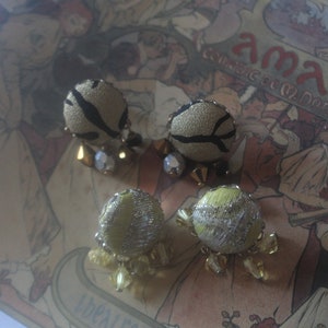 Könnte beinhalten: Vier Paar Vintage-Ohrringe. Zwei Paare sind beige mit schwarzen Akzenten und kristallartigen Perlen. Die anderen beiden Paare sind hellgrün mit silbernen Akzenten und kristallartigen Perlen. Die Ohrringe befinden sich auf einem Hintergrund im Vintage-Stil.