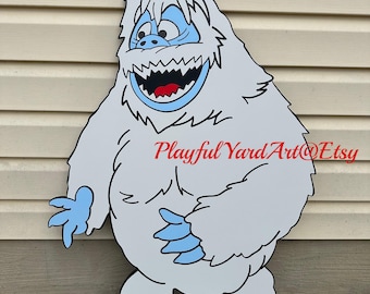 May include: A large, cartoon-style wooden cutout of a Yeti, with a light gray body, blue accents, and a wide, toothy grin. The Yeti has shaggy fur, blue hands and feet, and the text "Playful Yard Art@Etsy" in red.