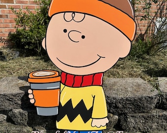 May include: Wooden yard art featuring a cartoon character wearing a brown and orange hat, a red scarf, and a yellow shirt with a black zig-zag design. The character is holding an orange coffee cup. The text "Playful Yard Art@Etsy" is at the bottom.