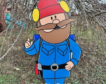 May include: A flat, cutout yard sign of a cartoon character wearing a red beanie, yellow earmuffs, and a blue uniform with a brown mustache. The character has a blue backpack, a black belt with a gray buckle, and black shoes. Text reads PlayfulYardArt@Etsy.
