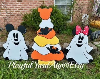 May include: Halloween yard decorations featuring Mickey and Minnie Mouse ghost figures and a candy corn-shaped tree. The decorations are painted in white, black, orange, and yellow. The text "Playful Yard Aty@Etsy" is at the bottom.