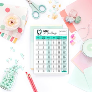 May include: A 52-week savings challenge printable with a teal header. The chart includes weekly deposit amounts and balance tracking. The image is styled with stationery, a flower, and decorative elements.