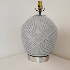 Op de afbeelding: Een witte keramische tafellamp met een waaiervormig ontwerp en een zilveren voet.