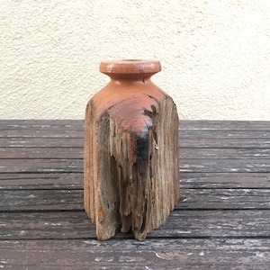 May include: A rustic wooden vase with a natural, weathered finish. The vase has a wide, round opening and a narrow base. It is made from a single piece of wood and has a unique, organic shape.