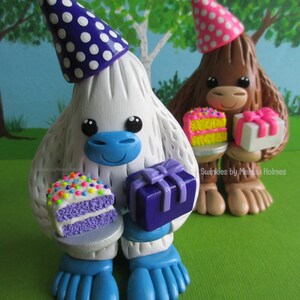 May include: Two whimsical figurines, one white and one brown, each wearing party hats and holding gifts and cake. The white figurine has a blue face and feet, and the brown one has a pink hat. The cake has colorful sprinkles.