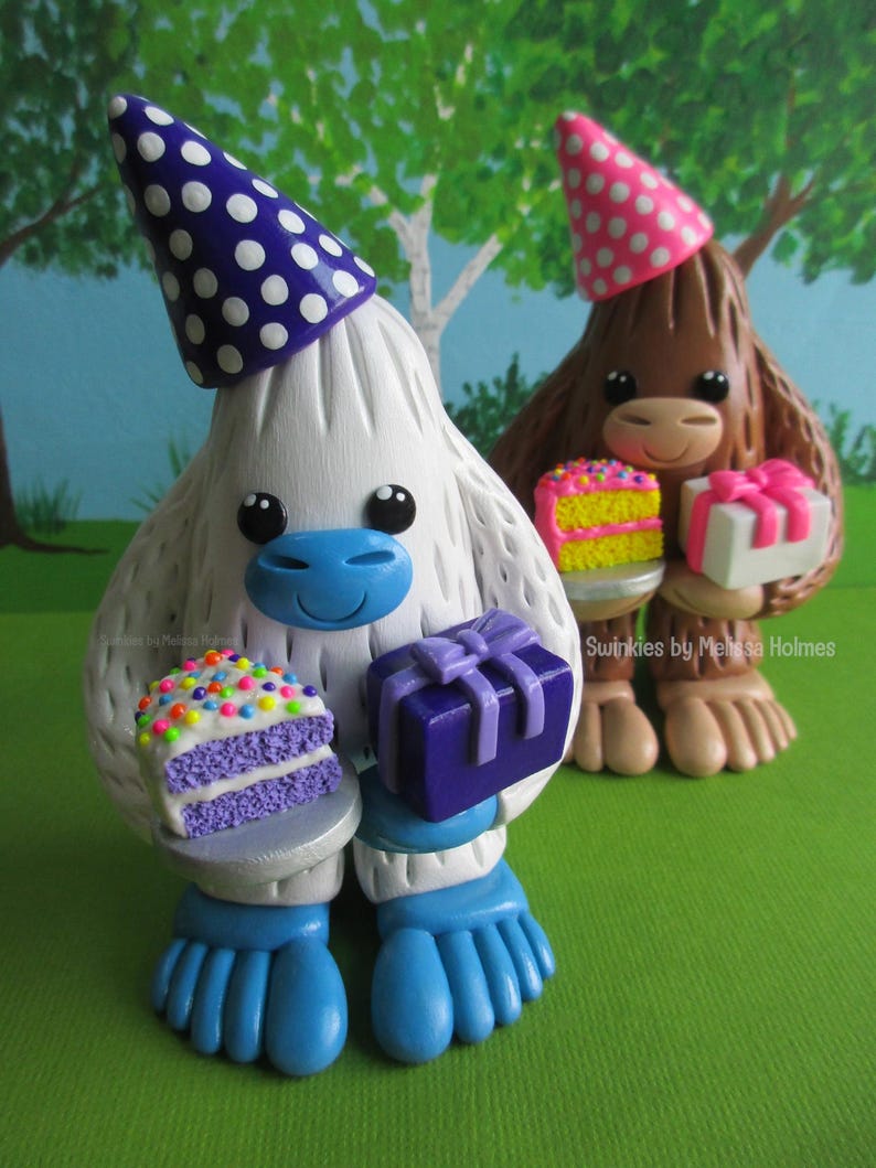 May include: Two whimsical figurines, one white and one brown, each wearing party hats and holding gifts and cake. The white figurine has a blue face and feet, and the brown one has a pink hat. The cake has colorful sprinkles.