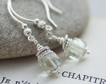 May include: A pair of silver earrings with green gemstone beads. The earrings are hanging from a silver hook and have a silver wire wrapped around the beads.