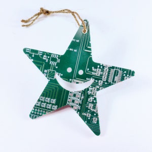 May include: A green circuit board shaped like a star with a smiley face cut out of the centre. The star has a brown twine string attached to the top for hanging.