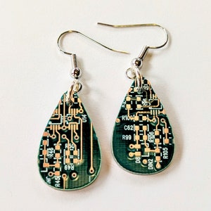 May include: A pair of teardrop-shaped earrings made from green circuit boards with silver hooks. The circuit boards have copper traces and text, including "R45", "R46", "R49", "R50", "014", "R100", "C62", "R99", "99", "D8", "296", "DIN2", "R106", and "R105".