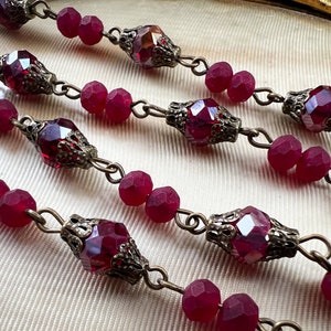 May include: A strand of red glass beads with ornate metal accents. The beads are connected by a silver chain.