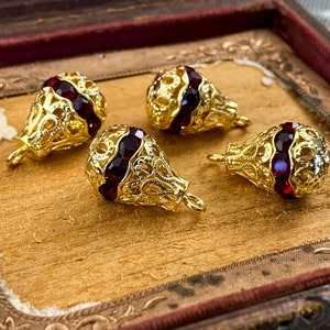May include: Four gold filigree teardrop-shaped pendants with red gemstone accents. The pendants have a delicate, intricate design and are perfect for adding a touch of elegance to any jewelry project.