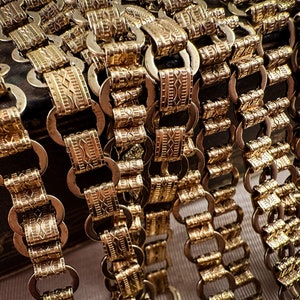 K&ouml;nnte beinhalten: Nahaufnahme von mehreren goldenen Ketten mit komplizierten, gemusterten Gliedern. Die Ketten sind in einer kaskadierenden Anordnung angeordnet, was einen strukturierten und luxuri&ouml;sen Look erzeugt.