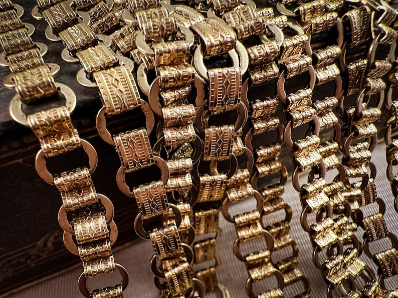 K&ouml;nnte beinhalten: Nahaufnahme von mehreren goldenen Ketten mit komplizierten, gemusterten Gliedern. Die Ketten sind in einer kaskadierenden Anordnung angeordnet, was einen strukturierten und luxuri&ouml;sen Look erzeugt.