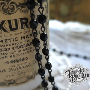 May include: A black beaded necklace with a silver chain. The necklace is draped over a vintage bottle with a label that reads "LUXUR COSMETIC MARVEL SUPERIOR TO COLD CREAM GUARANTEED NOT TO GROW AND NEVER BECOMES RANCID THE SIGN OF HARRIET HUBBARD AYER NEW YORK N.Y."