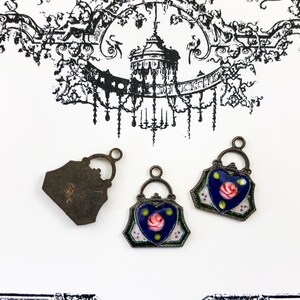 May include: Three antique-style metal charms in the shape of handbags. Two of the charms are decorated with blue enamel and a pink rose. The third charm is plain metal.