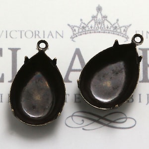 May include: Two antique bronze teardrop-shaped pendant settings with a smooth, rounded interior. The settings have a small loop at the top for attaching a chain or cord.