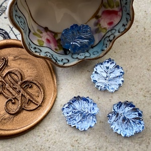 May include: Four blue glass leaf-shaped buttons with a raised design. The buttons are on a light brown surface.