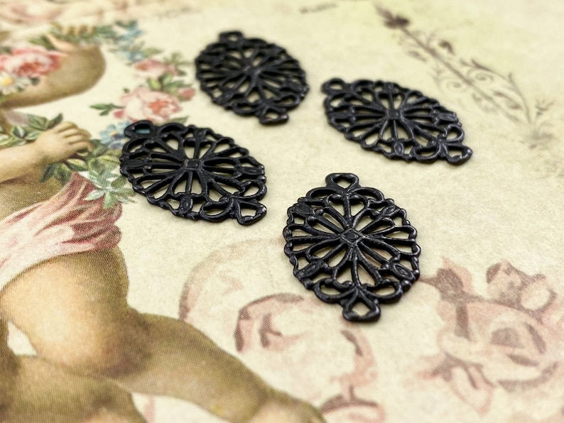Puede incluir: Cuatro abalorios ovalados de filigrana met&aacute;lica negra con un delicado dise&ntilde;o floral.