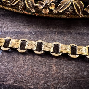 K&ouml;nnte beinhalten: Ein goldenes Kettenarmband mit geometrischem Muster. Die Kette besteht aus miteinander verbundenen ovalen Gliedern mit einem strukturierten Design.