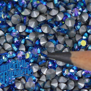 May include: A close-up image of a large quantity of small, round, iridescent blue rhinestones. The rhinestones have a silver backing and are arranged in a random pattern.