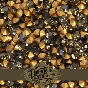 May include: A close-up image of a large quantity of small, round, gold and dark gray rhinestones. The rhinestones are scattered randomly and appear to be for crafting or jewelry making.