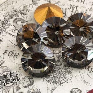 May include: Six clear glass faceted round buttons with a dark grey tint. The buttons are arranged in a circle on a white surface with black and white floral patterns. The word "FOR" is visible in the background.
