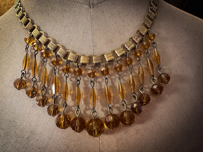 K&ouml;nnte beinhalten: Eine goldene Kettenkette mit einem Fransenbesatz aus bernsteinfarbenen Glasperlen.