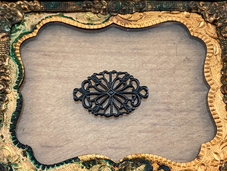 Puede incluir: Una filigrana decorativa de metal negro con un dise&ntilde;o floral, sobre un fondo dorado y verde.