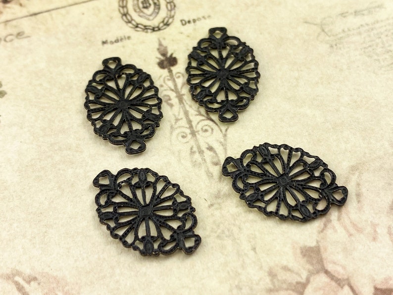 Puede incluir: Cuatro abalorios de filigrana de metal negro en forma ovalada con un dise&ntilde;o floral.