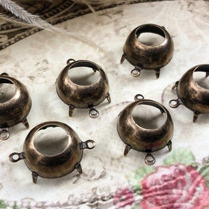 May include: Six antique gold-toned metal settings for cabochons. Each setting has a round opening and three prongs on the bottom.