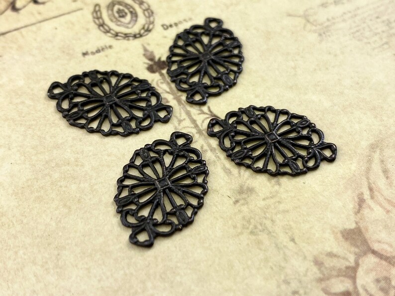 Puede incluir: Cuatro abalorios de filigrana de metal negro en forma ovalada con un dise&ntilde;o decorativo. Los abalorios tienen un acabado desgastado.