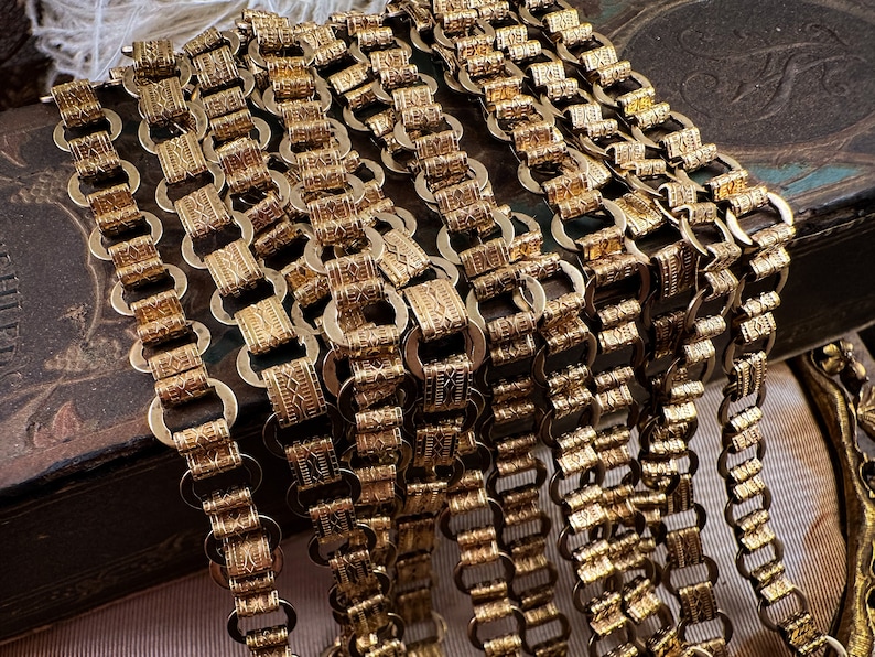 K&ouml;nnte beinhalten: Nahaufnahme mehrerer goldener Ketten mit komplizierten Designs. Die Ketten bestehen aus kleinen, miteinander verbundenen Ringen mit einer strukturierten Oberfl&auml;che. Die Ketten sind in einem mehrschichtigen Muster angeordnet, was ein optisch ansprechendes und luxuri&ouml;ses Aussehen erzeugt.